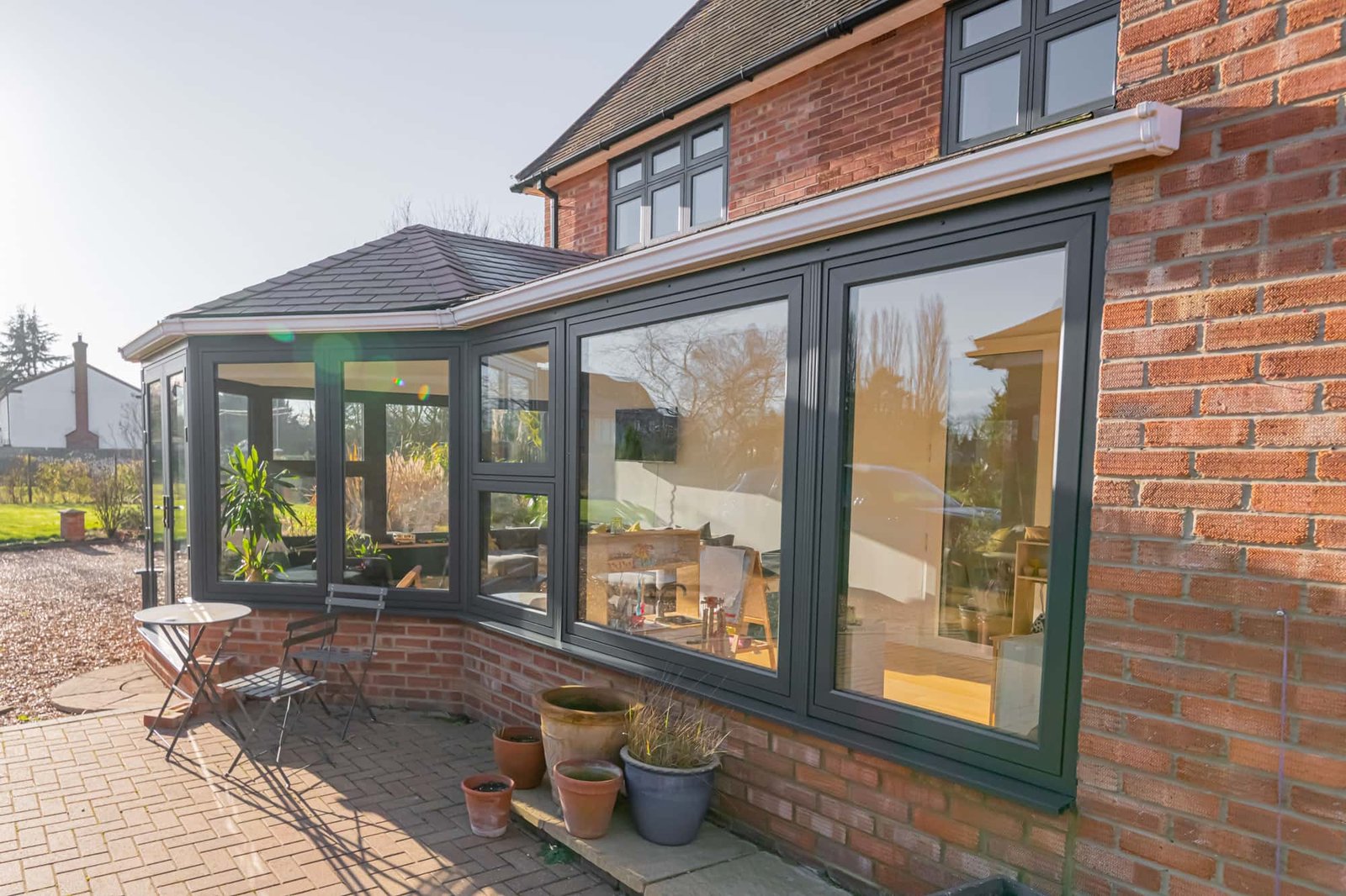 Grey-framed garden room beside a brick house